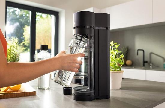 Hand benutzt einen schwarzen Wassersprudler auf Küchenarbeitsplatte