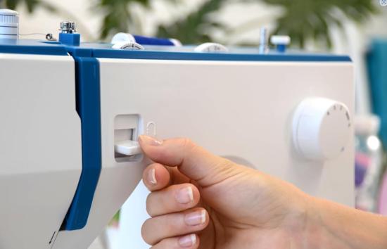 Eine Hand bedient die Einstellknöpfe einer Nähmaschine in Nahaufnahme