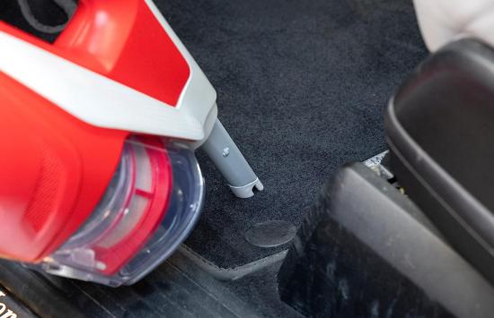 Ein roter Handstaubsauger reinigt den Autoteppich gründlich.