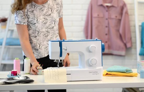 Person steht an einem Tisch mit Nähmaschine, Stoffen und Nähzubehör