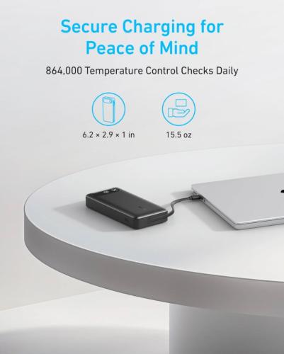 Schwarze Powerbank lädt Laptop auf rundem Tisch mit Sicherheitshinweisen.