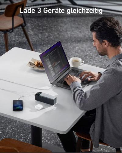 Mann arbeitet am Laptop und lädt Handy, Kopfhörer und Powerbank gleichzeitig auf.