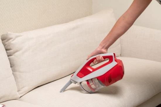 Person verwendet einen kabellosen Handstaubsauger auf einem beigen Sofa