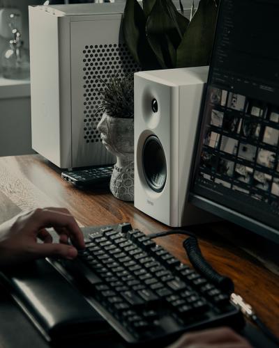Person am Schreibtisch mit Tastatur und modernem Computer-Setup, inklusive Lautsprechern und Pflanze