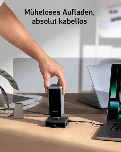 Hand platziert Smartphone auf kabellose Ladestation neben Laptop