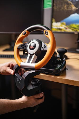 Gamer montiert orangefarbenes Lenkrad für Rennsimulationen an einem Schreibtisch vor einem Monitor