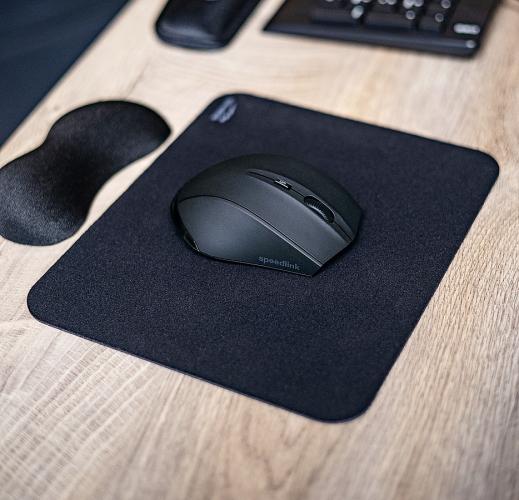 Schwarze Computermaus auf einem schwarzen Mauspad auf einem Holztisch neben einer Handballenauflage und einer Tastatur