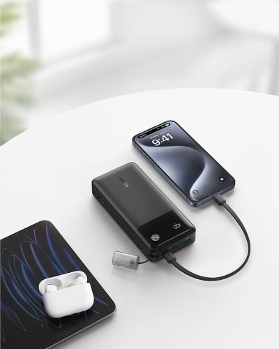 Ein Tisch mit einem Smartphone, das an eine Powerbank angeschlossen ist, kabellose Ohrhörer und ein Laptop
