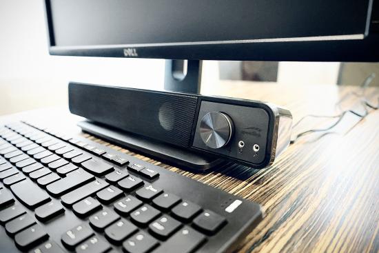 Soundbar mit Lautstärkeregler neben einem Computerbildschirm und Tastatur auf einem Schreibtisch